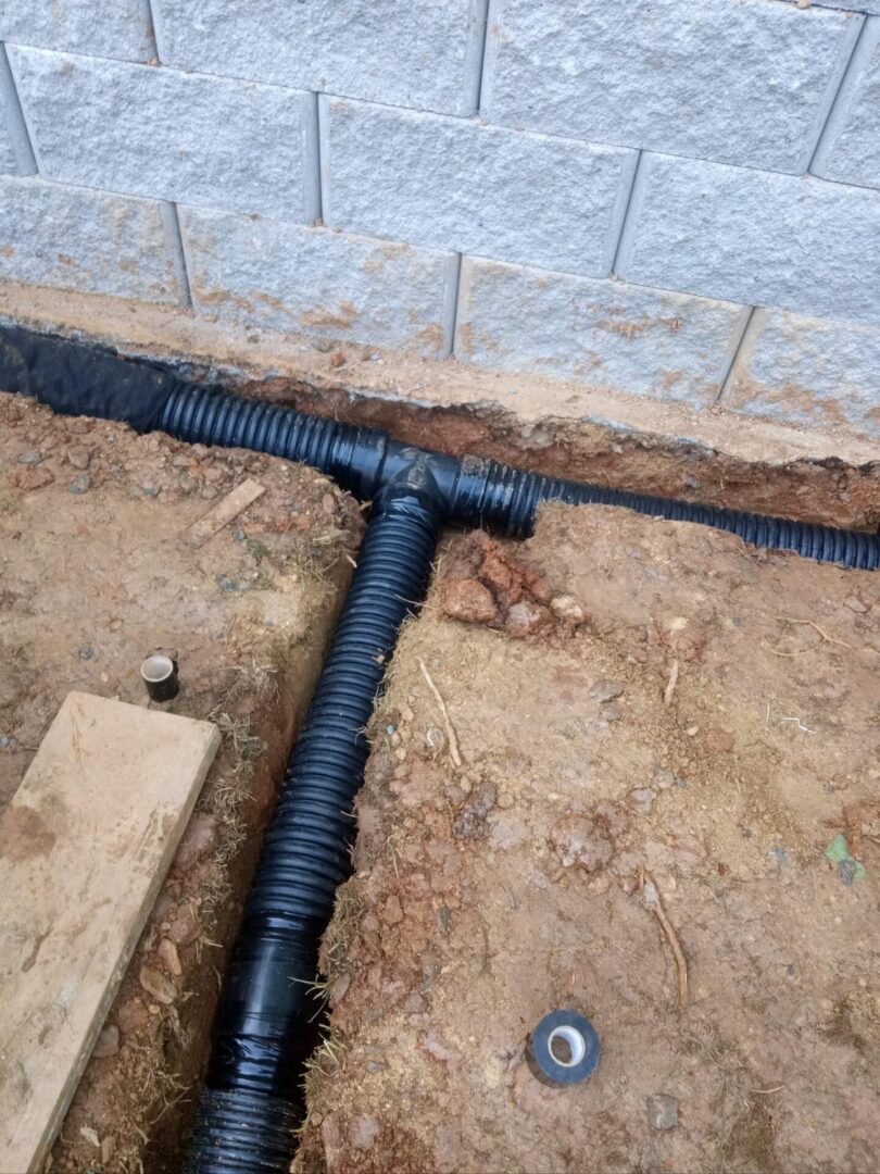 A black pipe laying on the ground next to a brick wall.